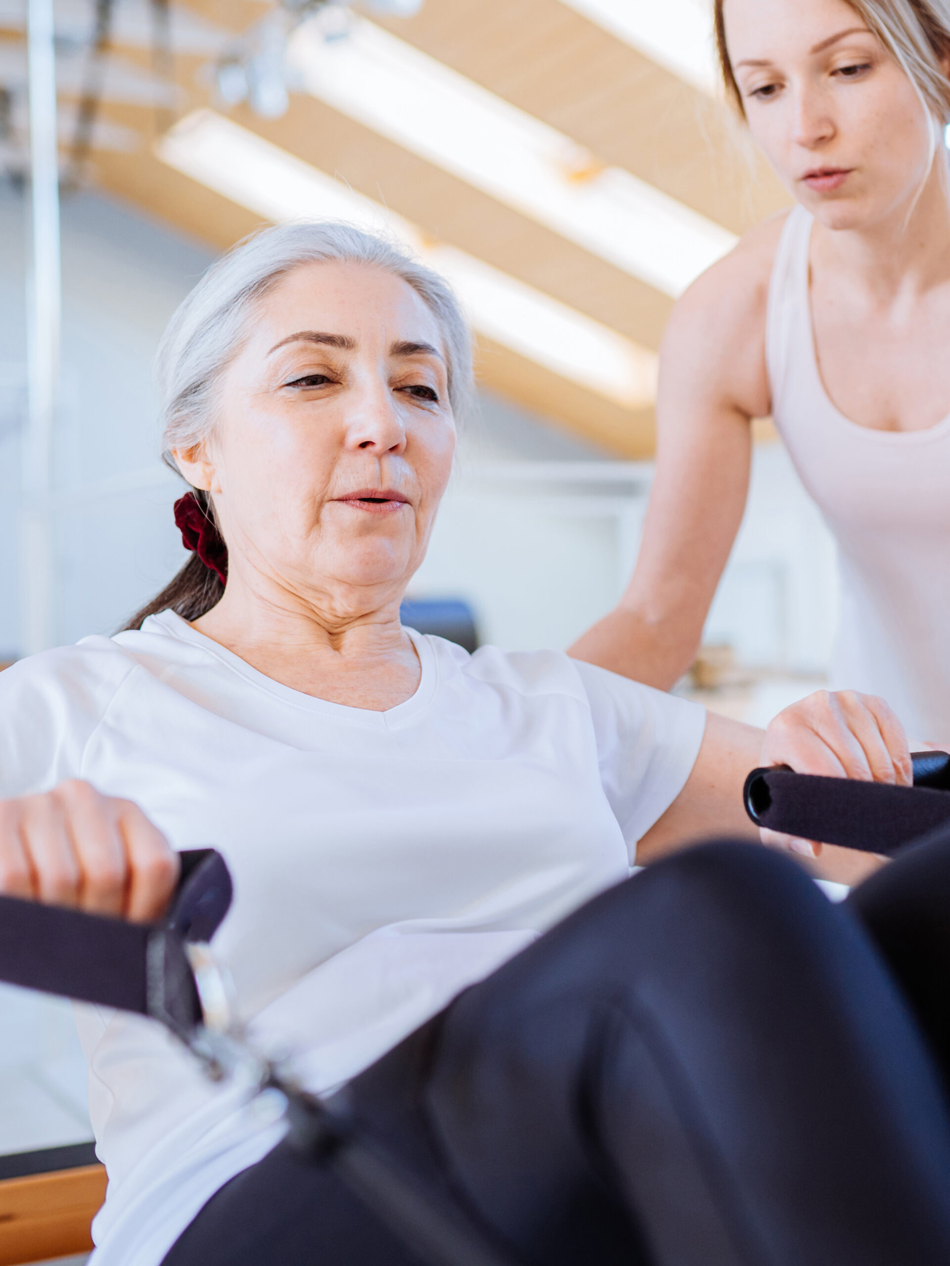 Personal Trainer Assist Senior Woman Exercising On Machine At Gym